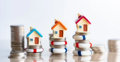 Small houses are perched on stacks of coins, symbolizing wealth and investment in real estate