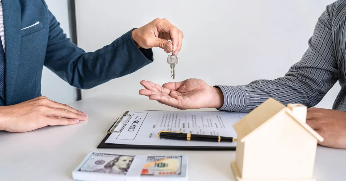 A man handing a key into another man’s hand with a contract paper placed on table