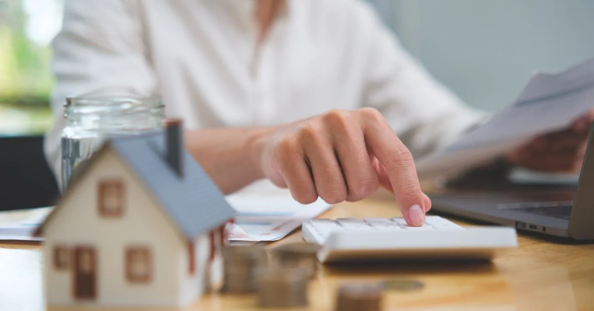 A person using a calculator with a small house mockup nearby