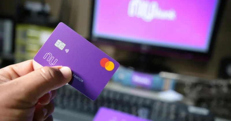 A close-up of a hand holding a purple bank card in front of a computer screen