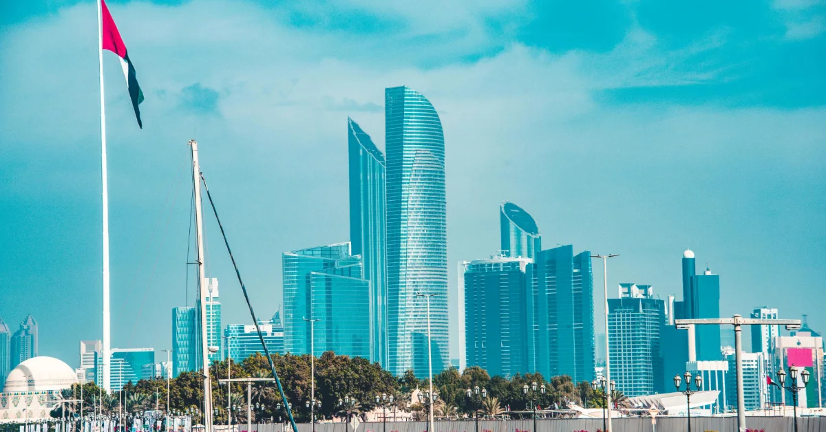 أفق مدينة أبوظبي مع ناطحات السحاب اللامعة والعلم الإماراتي يرفرف في السماء الزرقاء.