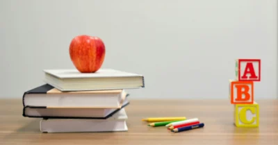 ABC blocks are placed on the table beside an apple resting on top of a stack of books