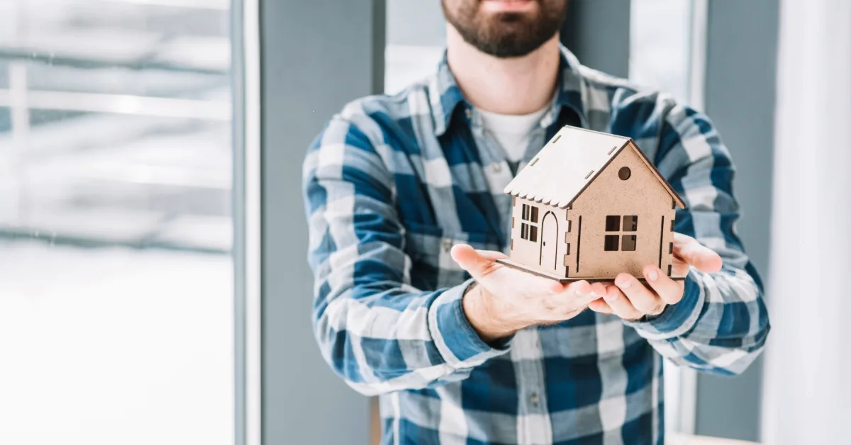 شخص يحمل مجسم منزل من الخشب