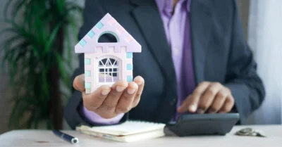 A man in a suit holding a miniature house model