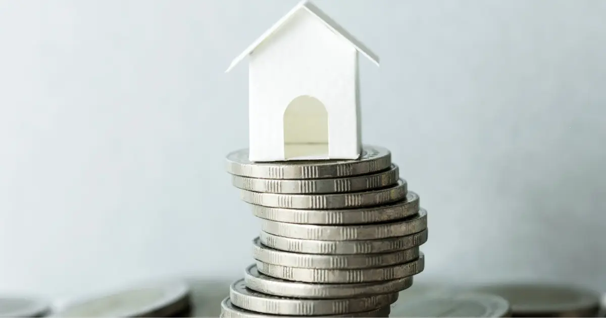 مجسم منزل صغير موضوع فوق كومة من النقود