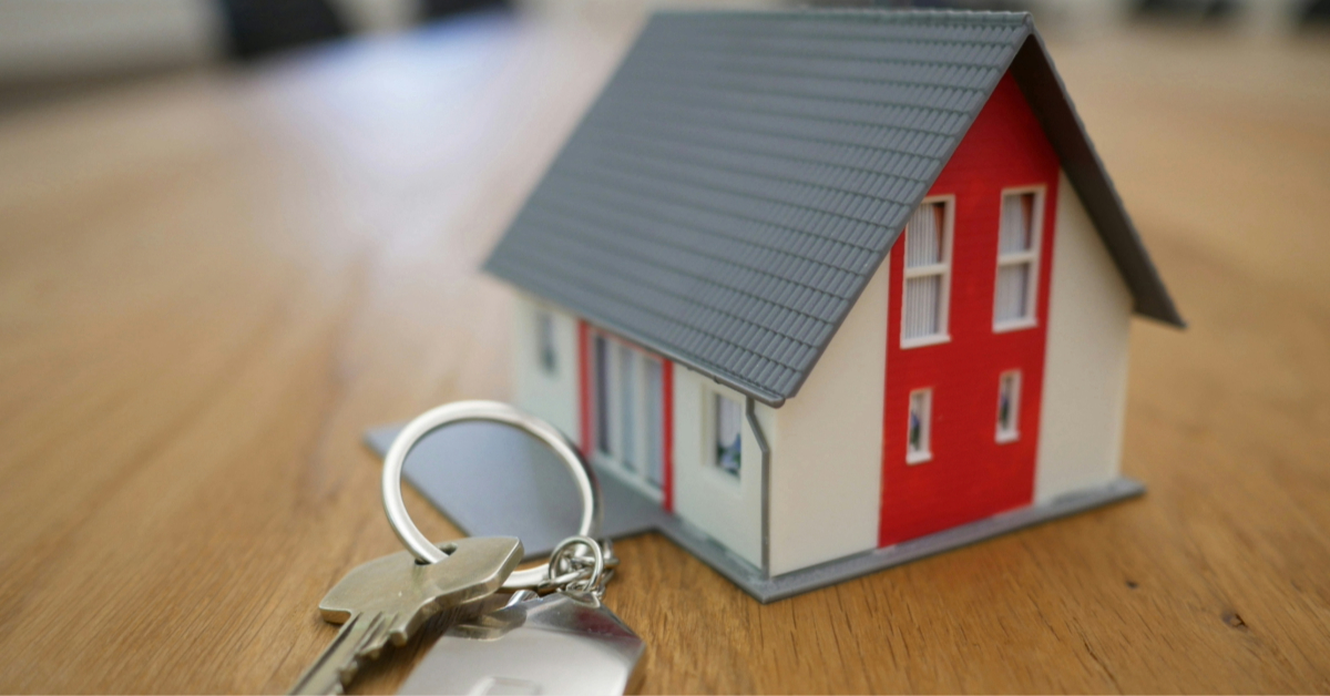 A white and red miniature house placed on a table with keys beside it