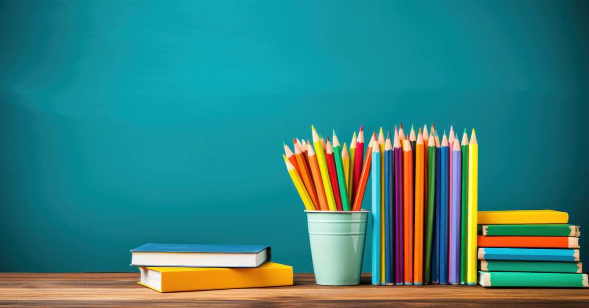 Pencils in a wire holder on books near a chalkboard back to school