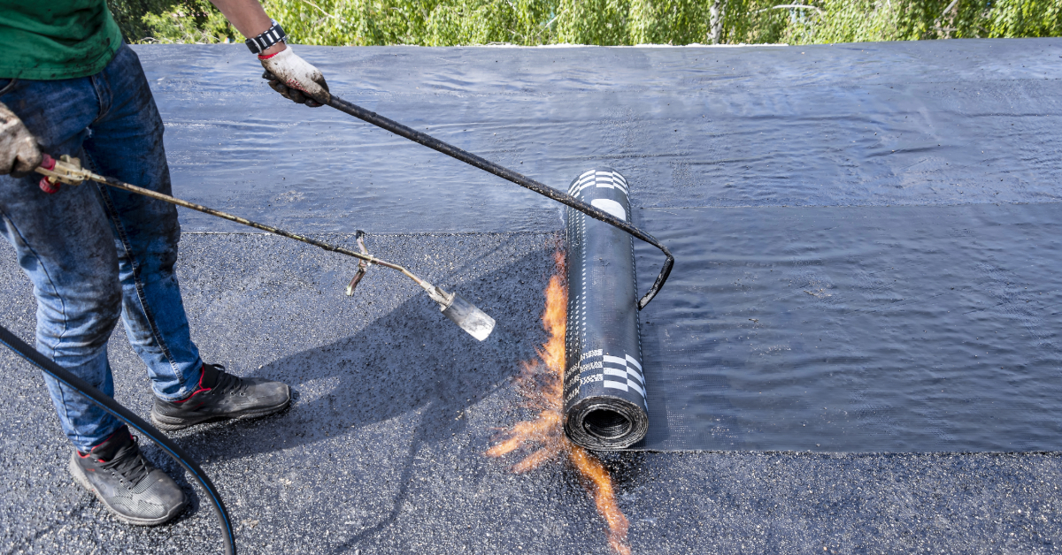 Builder putting waterproofing material on the roof of a multi-story residential building using a gas burner.