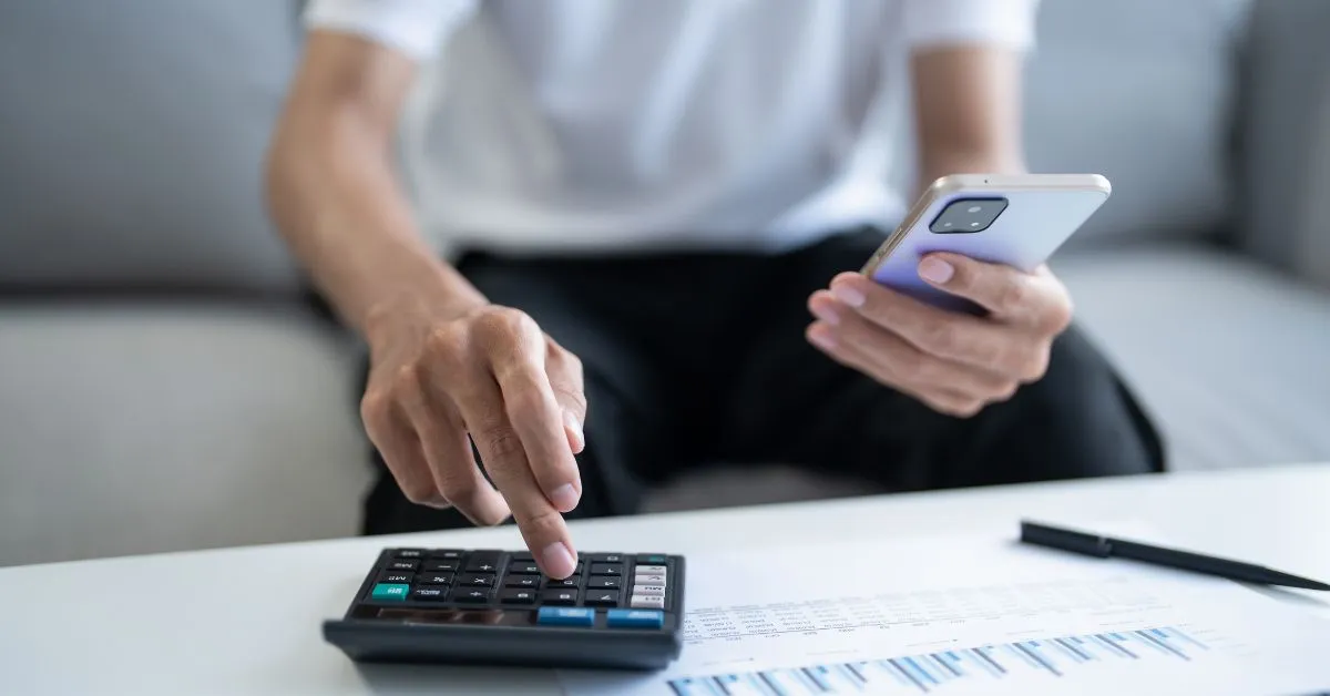 A man using a calculator and holding a phone in his other hand