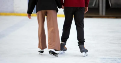 A waist-down shot of a boy and girl ice skating, showing their legs and skates gliding on the ice