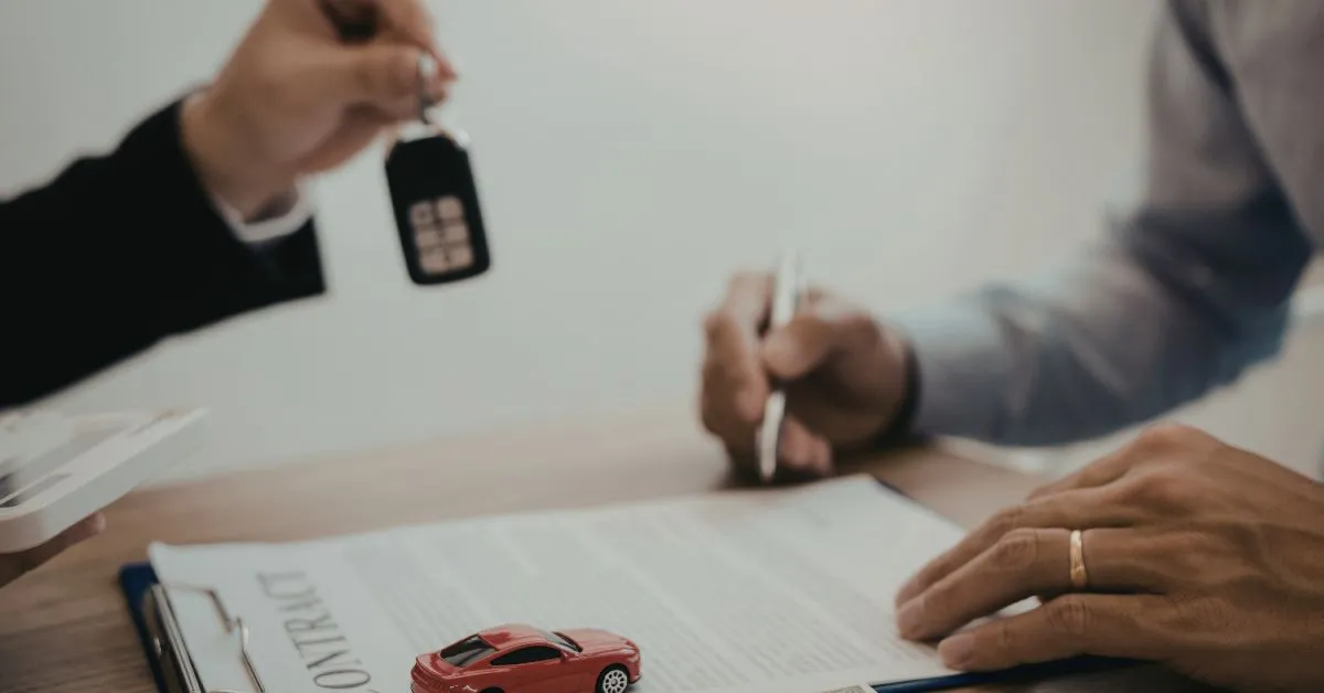 A man handing off car keys to a customer signing a contract