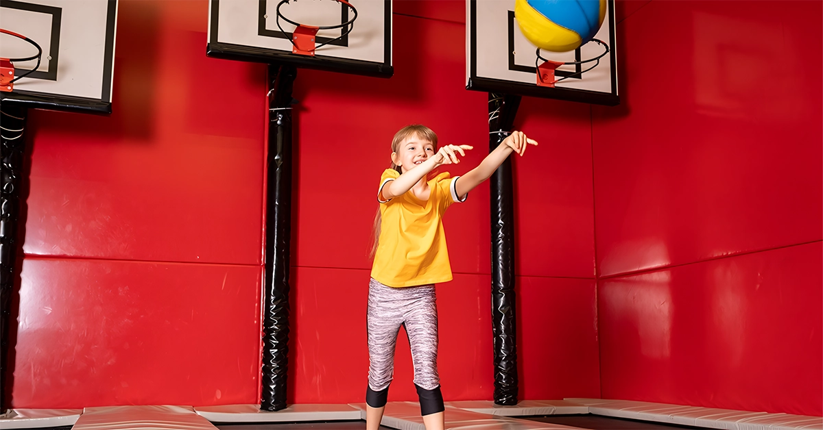 A kid playing basketball in a Trampo park