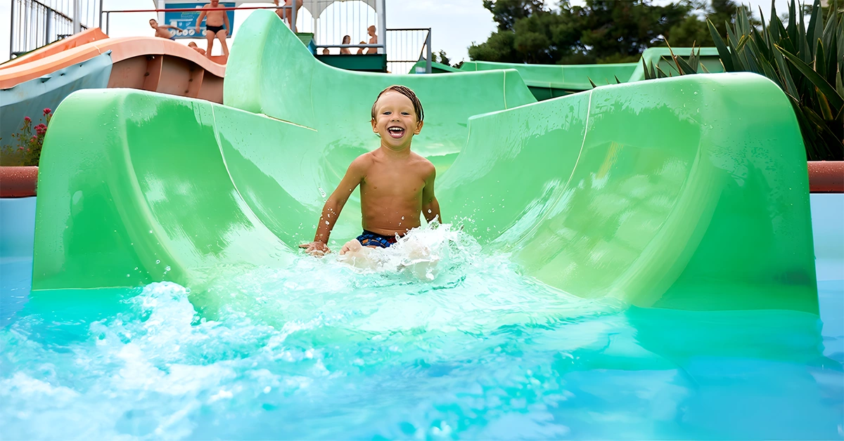 A young boy gliding down a green slide at Lapita, Dubai Parks and Resorts