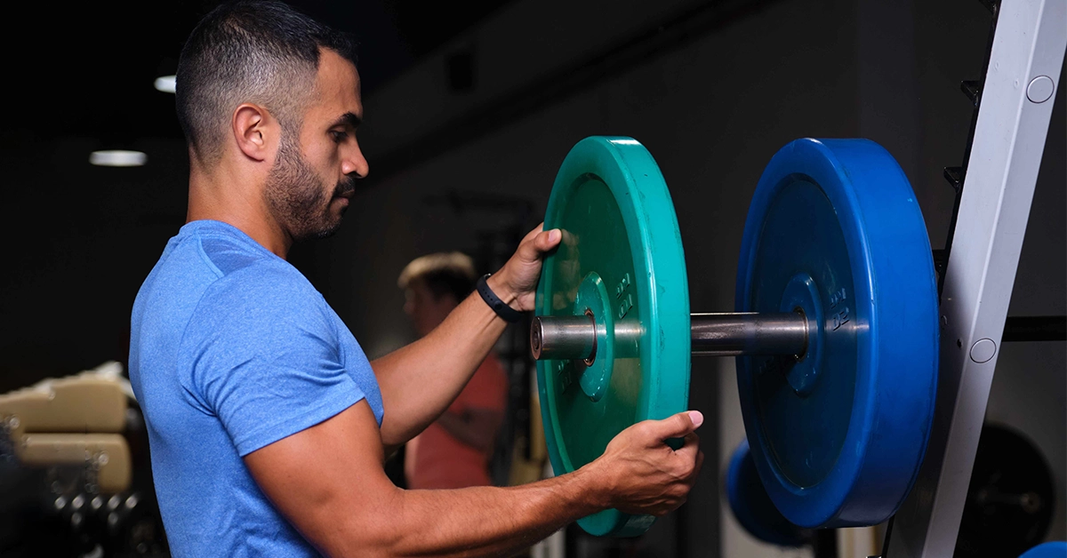 A man adjusting weights at a popular gym in Karama)