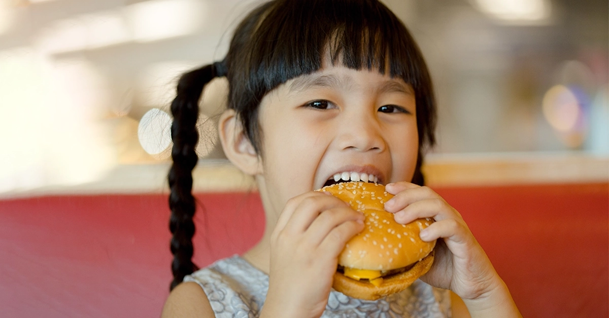 A Child eating chicken cheese burger at a food court
