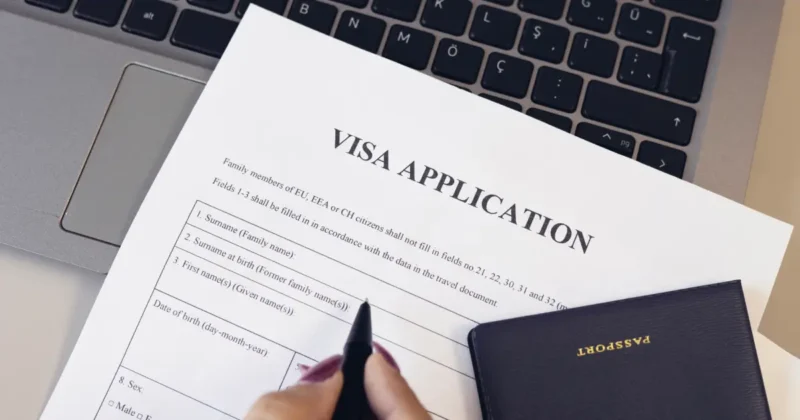 Woman completing visa application with pen, passport, and computer