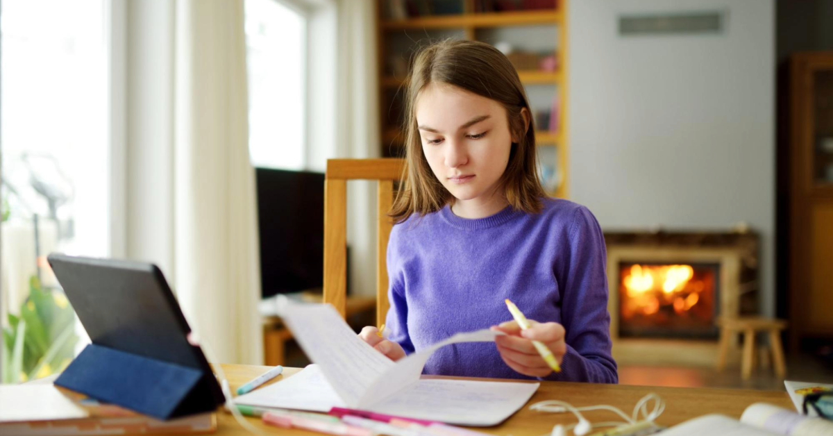 kid studying on both a workbook and an ipad