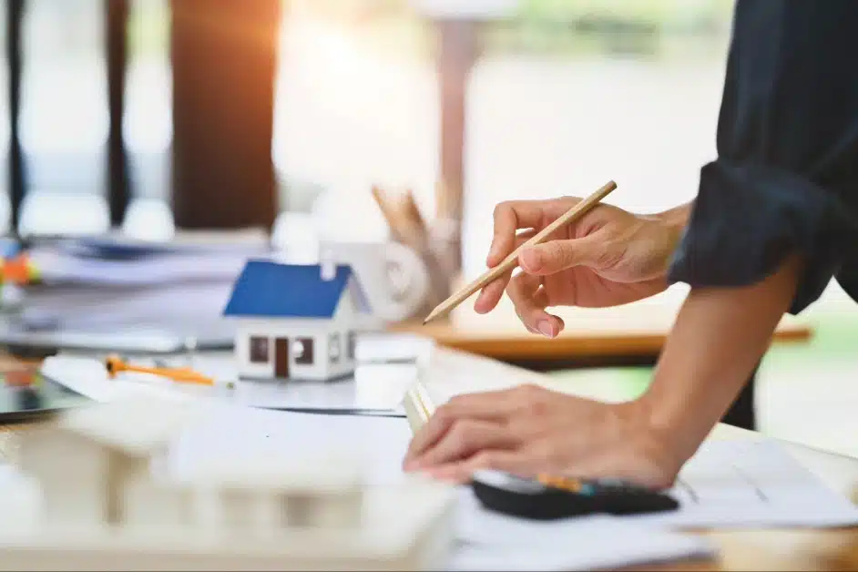 A miniature house model with a finger pointing at a property contract