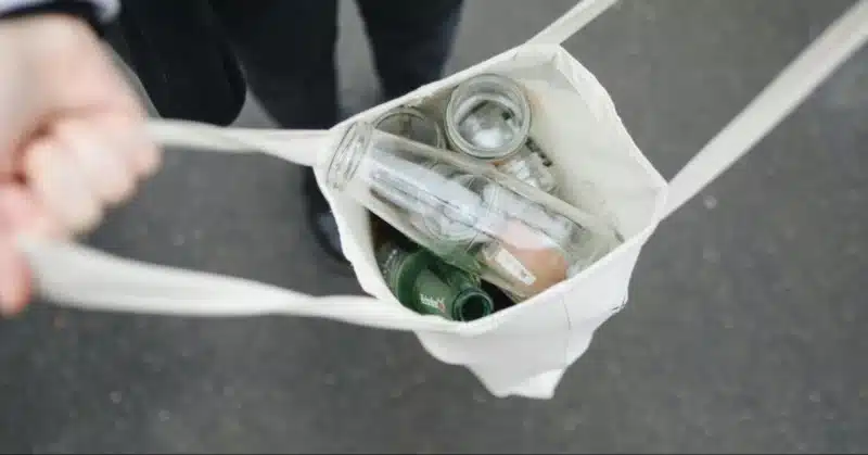 Alt text: Person holding a bag full of glass bottles to show What things can we recycle at home