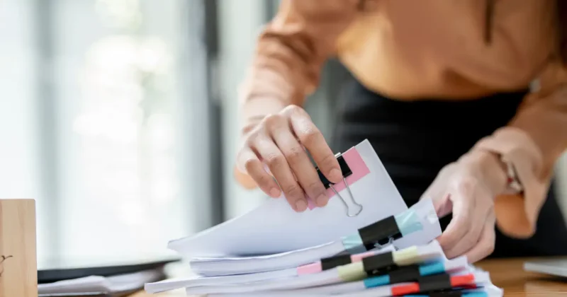 Businesswoman sorting and checking paperwork at a busy office desk