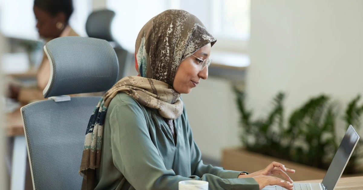 A Woman Wearing Hijab Sitting on a Chair while Busy Working on Her Laptop