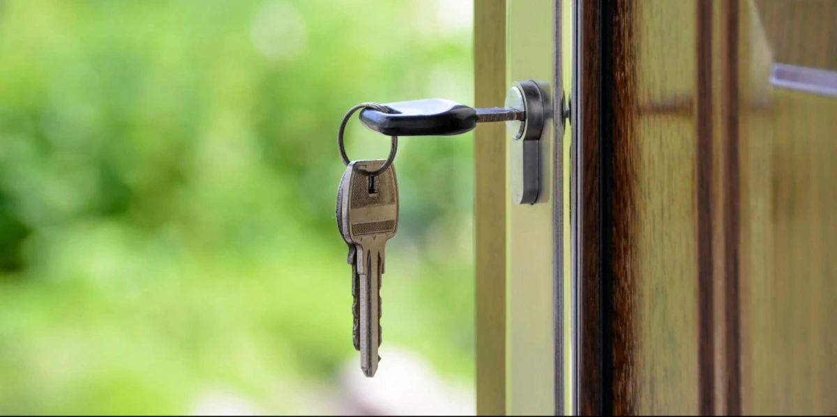 A key is inserted into the lock of a slightly open wooden door