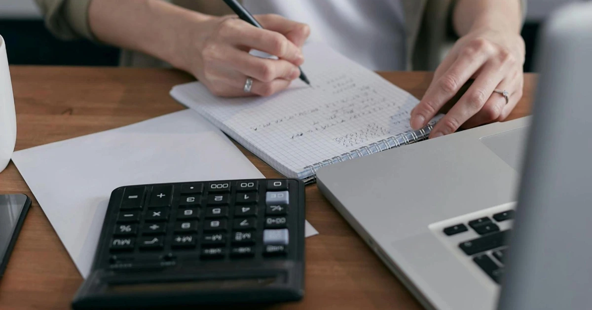 Person taking notes with a pen and calculator - cost of living