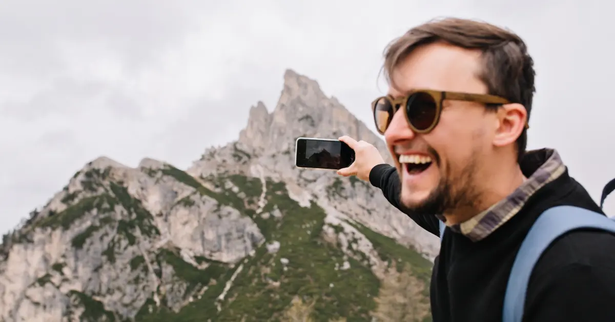 man in sunglasses taking a picture on the mountain