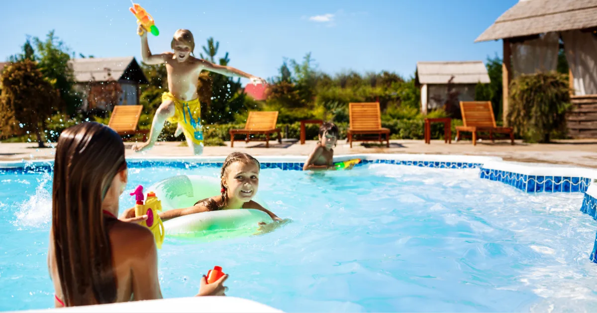 Cheerful children playing waterguns, rejoicing, jumping, swimming in pool