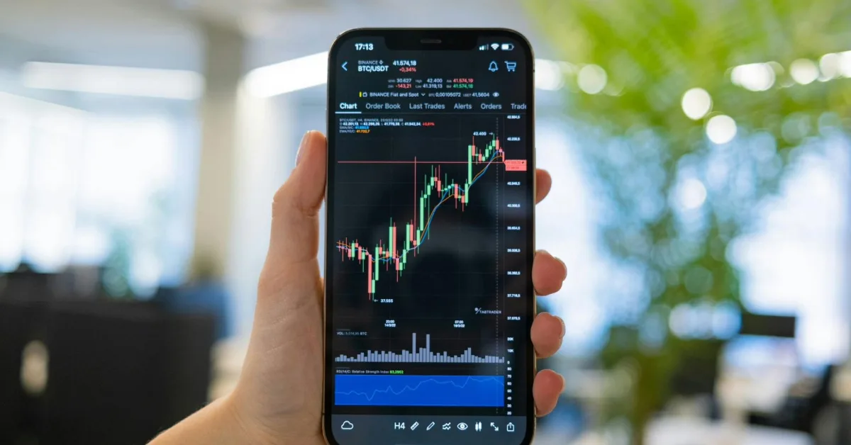 Hand holding a smartphone showing a stock trading chart