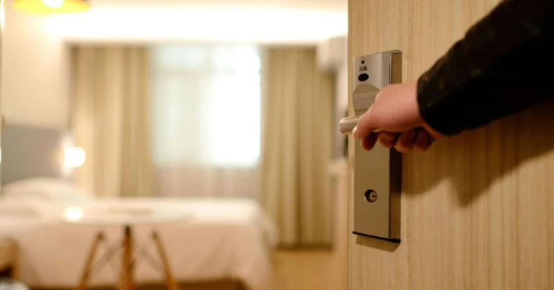 Hand opening a hotel room door with an electronic lock