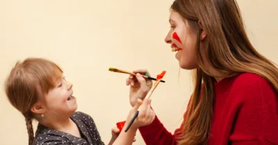 Happy woman and girl with down syndrome painting each other's faces