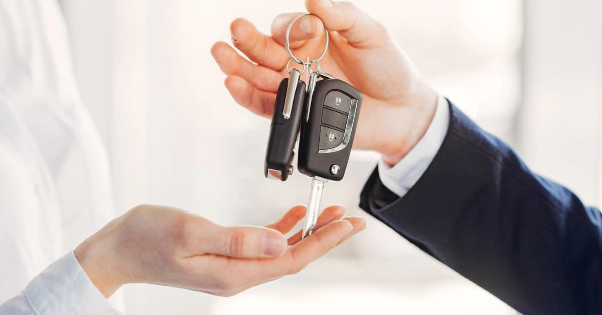 A car dealer handing over the keys to a woman who purchased a car.