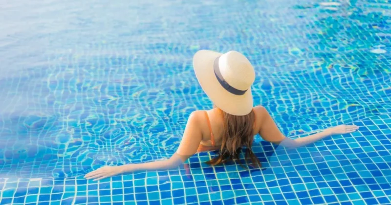 A woman enjoying her pool day, wearing a large sun hat to shield herself from the sun.