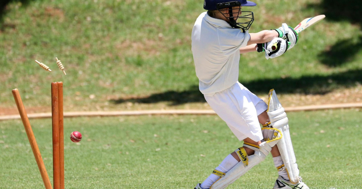 Boy in cricket gear batting as the ball hits the wicket