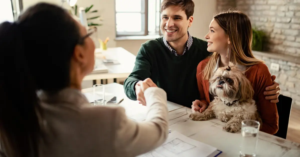 Happy couple with a dog shaking hands with real estate agent in the office