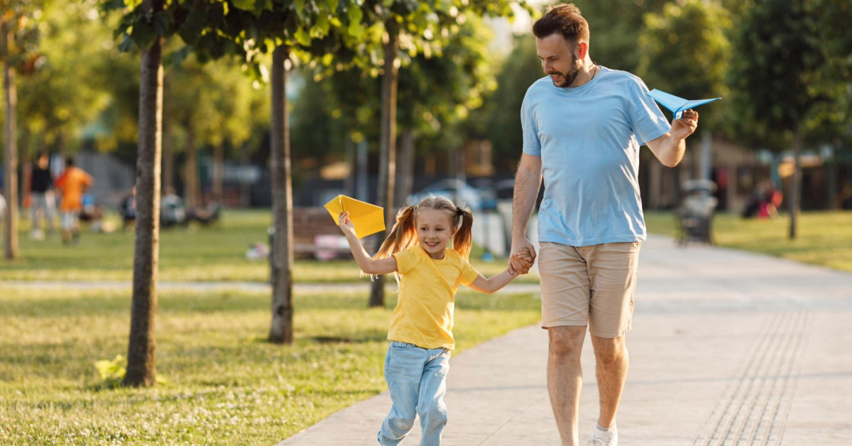 A father-daughter duo enjoying their time in the park, flying paper planes