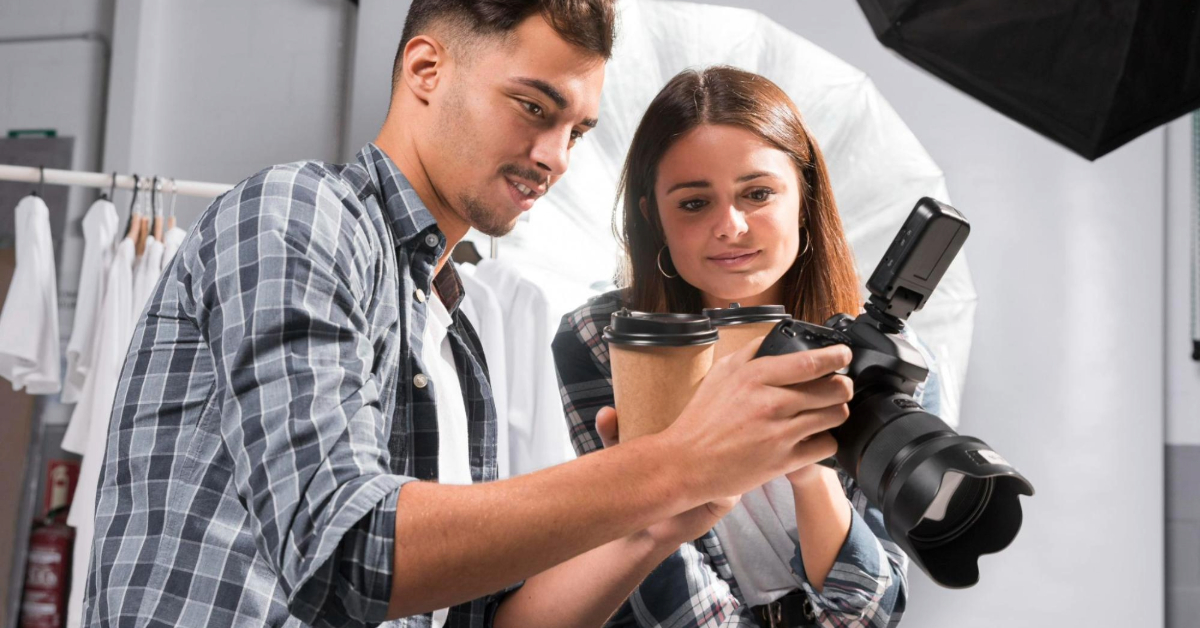 A man holding a coffee cup in one hand and a camera in the other, showing photos to a woman