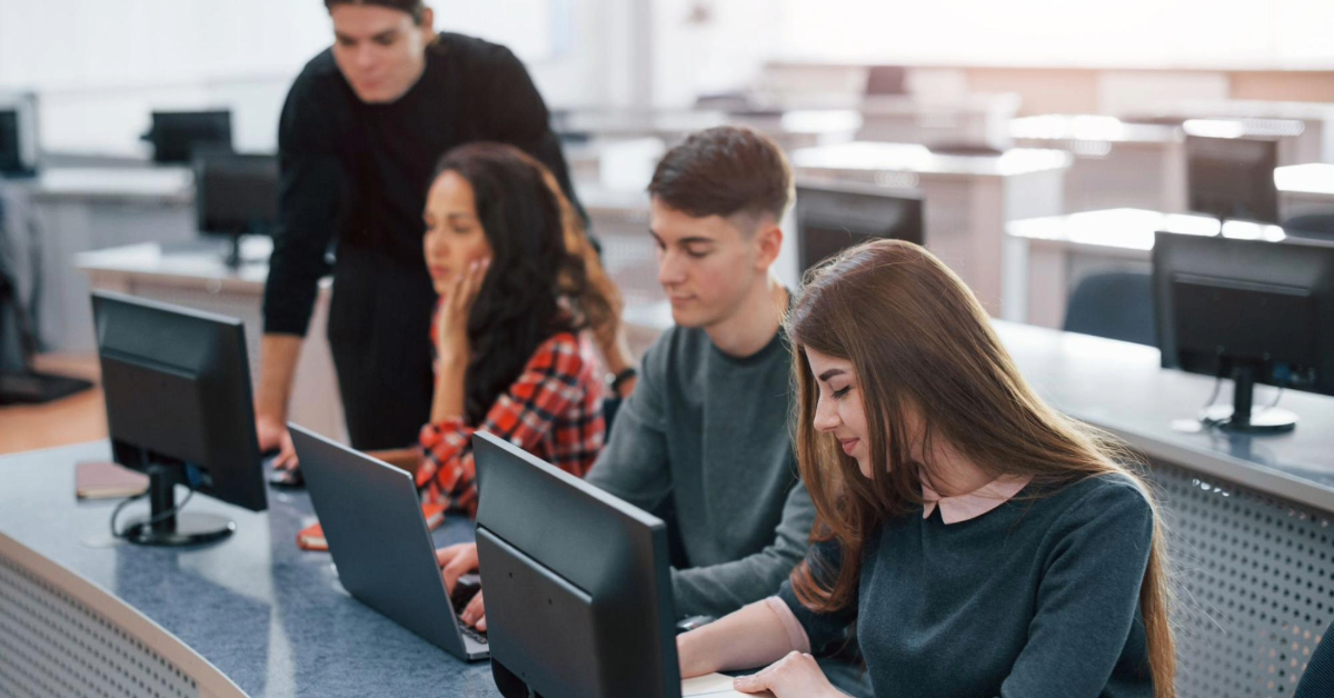 Three students in a computer lab with an instructor teaching and guiding them