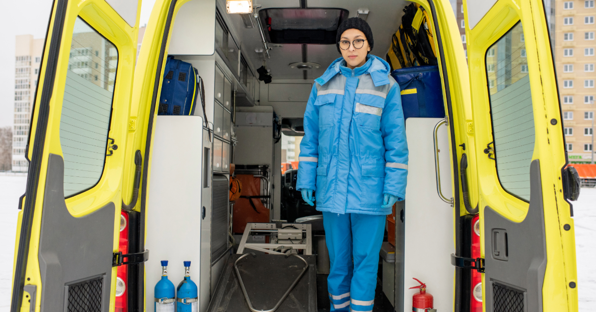Young female paramedic in uniform standing by an empty stretcher in an ambulance car