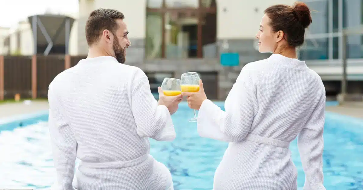 A couple clinking glasses and doing a cheers by the pool, enjoying a sunny day