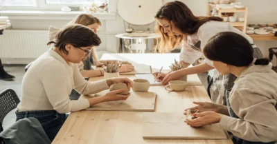 Portrait of young woman teaching apprentices making ceramics in pottery workshop