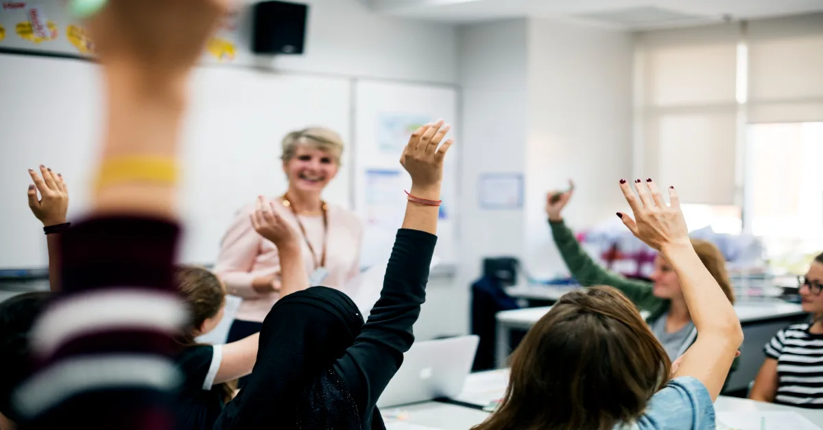 Students with their hands up responding to their teacher
