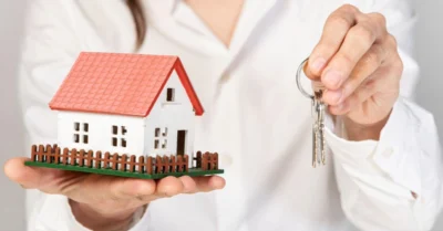 A woman holding a toy house in one hand and the keys to a home in Dubai