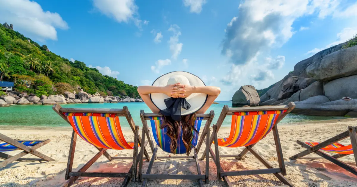 Woman with hat sitting on chairs on a beautiful tropical beach