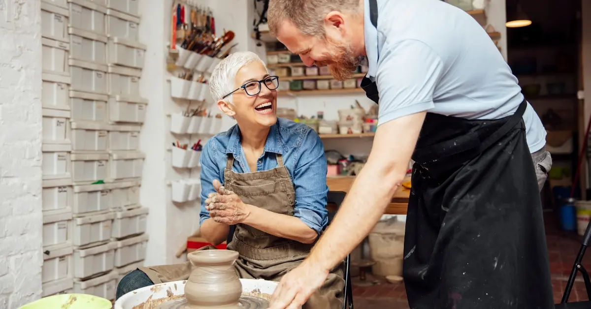 woman spinning clay on a wheel with teacher at pottery class