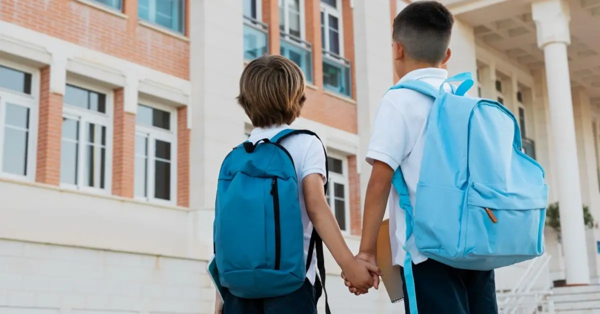 طفلان يحملان حقائب مدرسية ويقفان أمام مبنى مدرسة حديثة في دبي