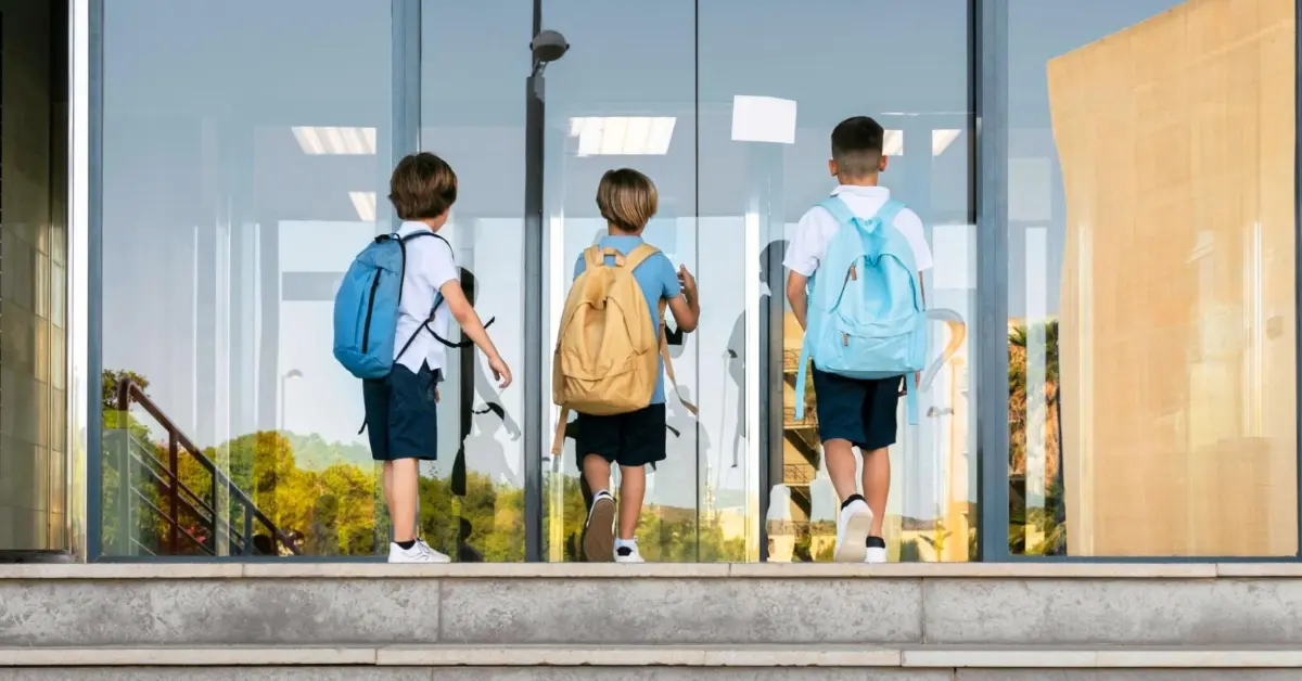 مجموعة طلاب صغار يدخلون المدرسة حاملين حقائبهم، في بيئة تعليمية منظمة تعبّر عن الاستعداد للعام الدراسي الجديد
