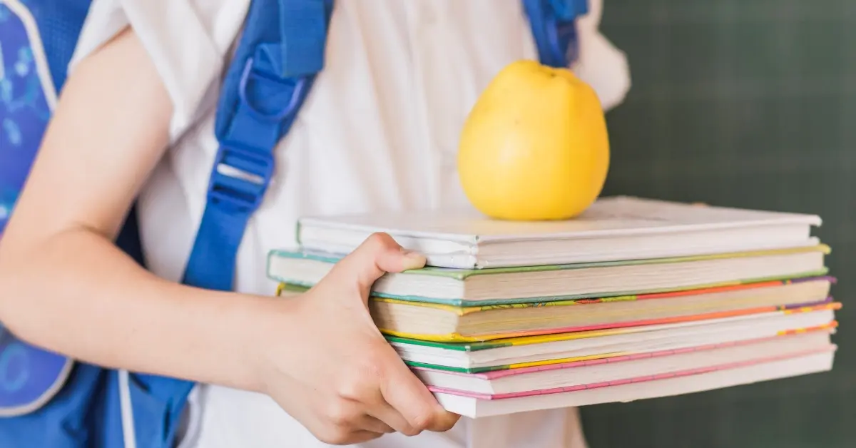 A kid holding textbooks and an apple