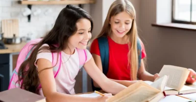 Happy schoolgirls with backpacks sitting at desk